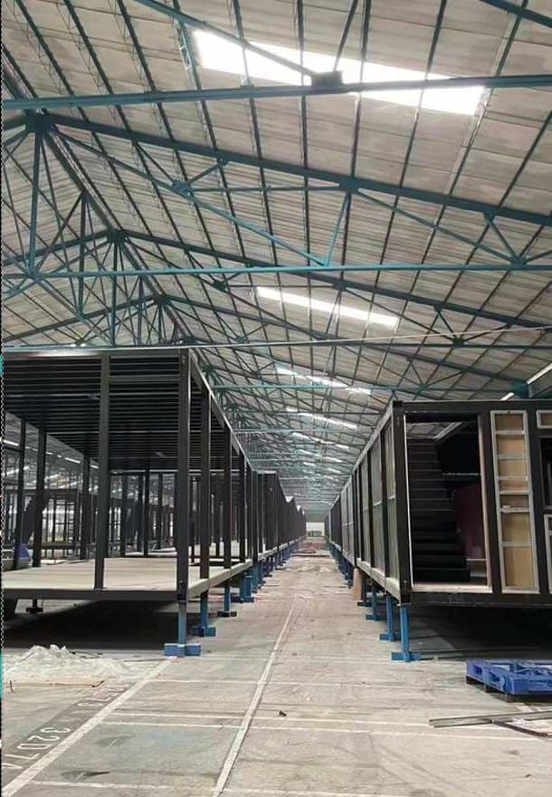 Rows of steel module frames on stands inside a factory hall, lit by skylights.